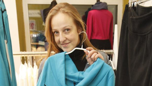 Eine Frau hält einen türkisfarbenen Blazer auf einem Kleiderbügel in einem Bekleidungsgeschäft.