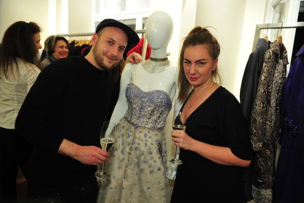 Ein Mann und eine Frau posieren mit Champagner neben einer Schaufensterpuppe mit einem verzierten Kleid.