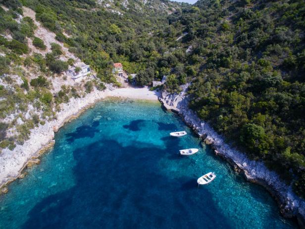 Drei Boote ankern in einer kleinen Bucht mit türkisfarbenem Wasser.