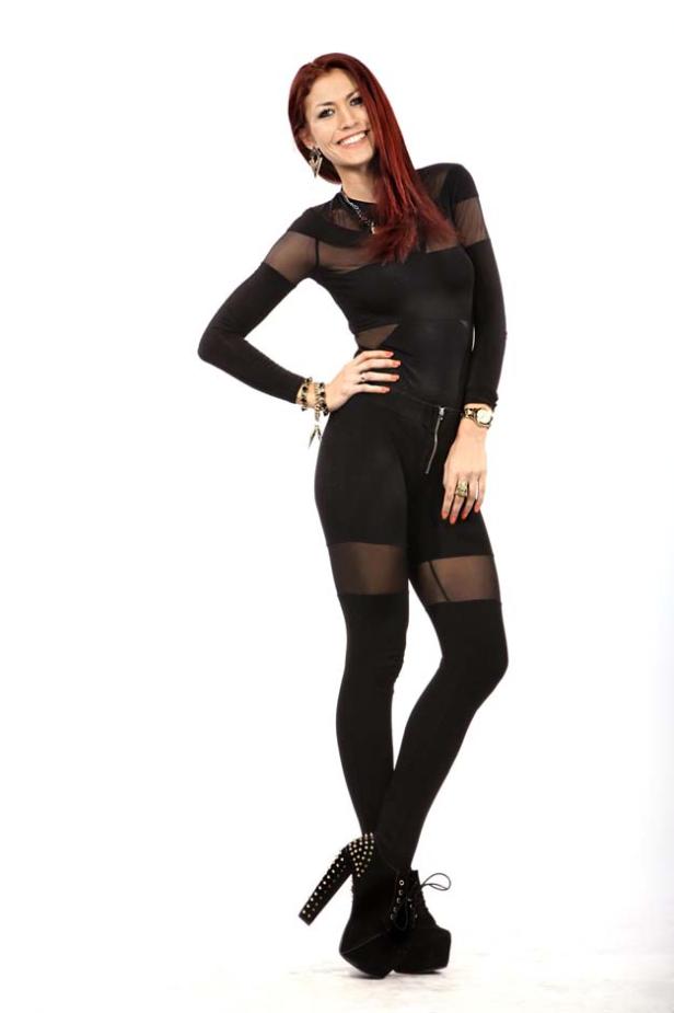 Eine Frau mit roten Haaren posiert in einem schwarzen Outfit und Plateauschuhen.