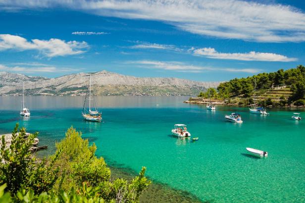 Mehrere Boote ankern in einer türkisfarbenen Bucht vor einer bewaldeten Küste.