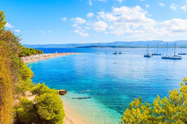 Blick auf den Strand Zlatni Rat (Goldenes Horn) in Kroatien mit vielen Badegästen und Segelbooten.