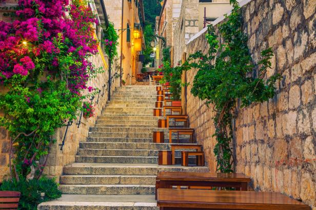 Eine steile Treppe mit Tischen und Stühlen führt durch eine Gasse hinauf.