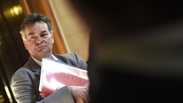 Ein Mann im Anzug hält eine rote Akte in seinen Händen.