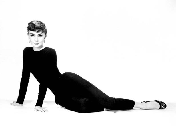 Audrey Hepburn posiert in einem schwarzen Overall auf dem Boden.