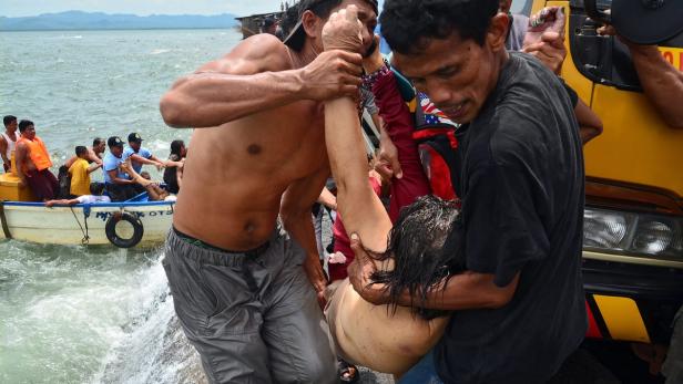 Helfer tragen eine bewusstlose Person an Land, während andere in einem Boot warten.