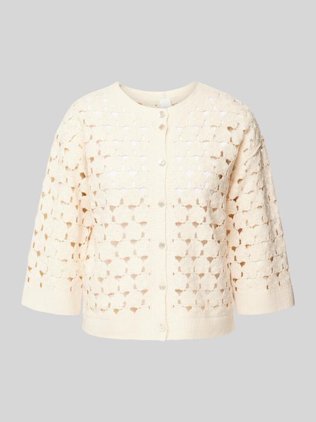 Eine cremefarbene, gehäkelte Strickjacke mit drei Viertel Ärmeln.
