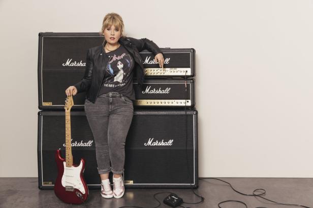 Eine Frau mit Gitarre posiert vor drei Marshall-Verstärkern.