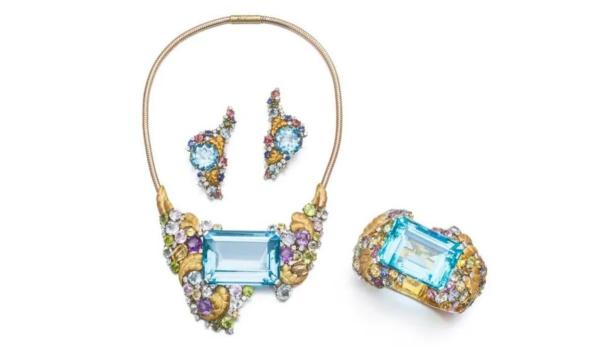 Ein Schmuckset mit Halskette, Ohrringen und Ring, besetzt mit hellblauen und bunten Edelsteinen.