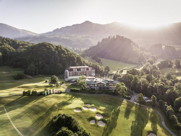 Das Grand Tirolia Hotel liegt in Kitzbühel auf einem Golfplatz vor einer Bergkulisse.