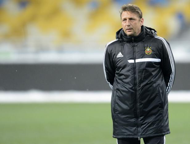 Ein Mann in einer schwarzen Adidas-Jacke steht auf einem Fußballfeld.