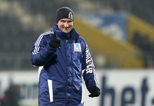 Ein lächelnder Mann mit Mütze und Winterjacke zeigt mit dem Finger nach oben.