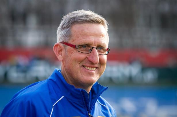 Ein lächelnder Mann mit Brille und blauer Jacke.
