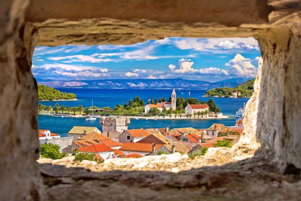 Blick durch eine Steinöffnung auf eine Insel mit Häusern und einer Kirche am Meer.