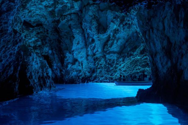 Ein Boot mit Touristen in einer blau beleuchteten Höhle.