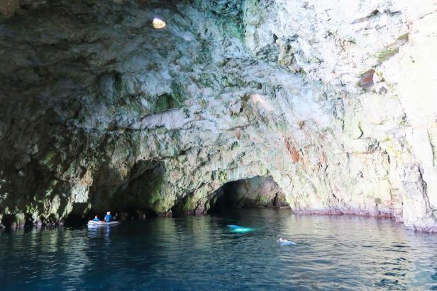 Menschen erkunden eine Höhle mit dem Boot und schwimmend.