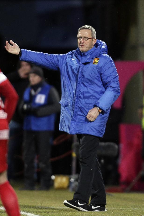 Ein Trainer in blauer Jacke gestikuliert am Spielfeldrand.