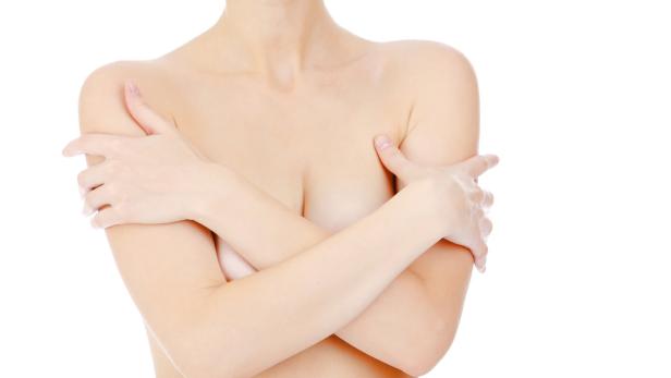 Eine Frau mit hellen Haut bedeckt ihre Brust mit ihren Armen.