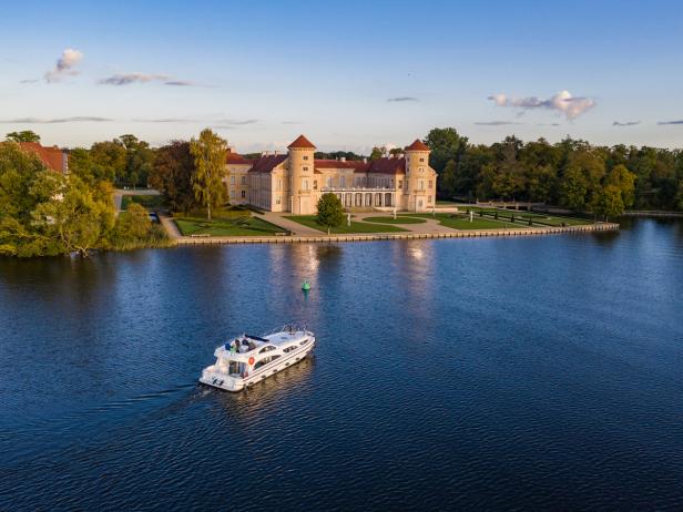 Ein Motorboot fährt auf einem See vor dem Schloss Rheinsberg.