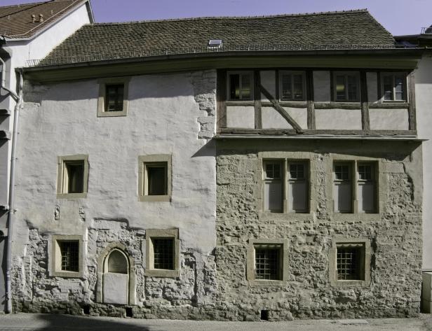 Ein altes, zweistöckiges Gebäude mit einer Mischung aus Putz- und Steinmauerwerk.
