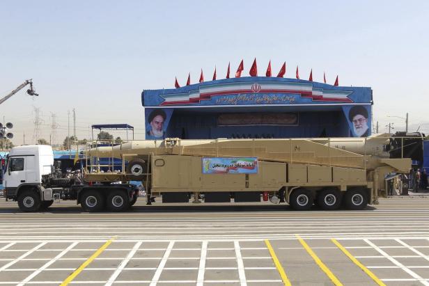 Ein iranischer Lastwagen transportiert eine Rakete vor einer Tribüne mit Porträts von Ajatollah Khomenei.