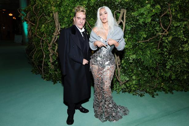 Kim Kardashian posiert mit einem Mann vor einem grünen Hintergrund.