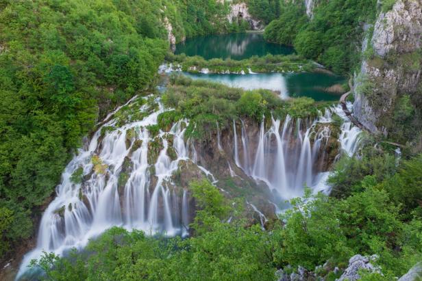 Ein Wasserfall ergießt sich in Kaskaden in einen smaragdgrünen See, umgeben von üppigem Grün.