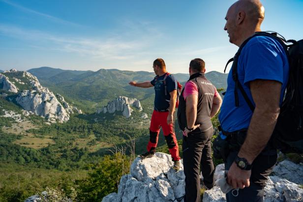 Drei Wanderer genießen die Aussicht auf eine grüne Hügellandschaft.