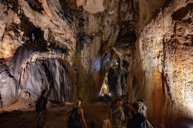 Eine Gruppe von Menschen erkundet eine große Höhle mit Stalaktiten und Stalagmiten.