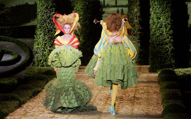 Zwei Models präsentieren extravagante grüne Kostüme auf einem Laufsteg im Freien.