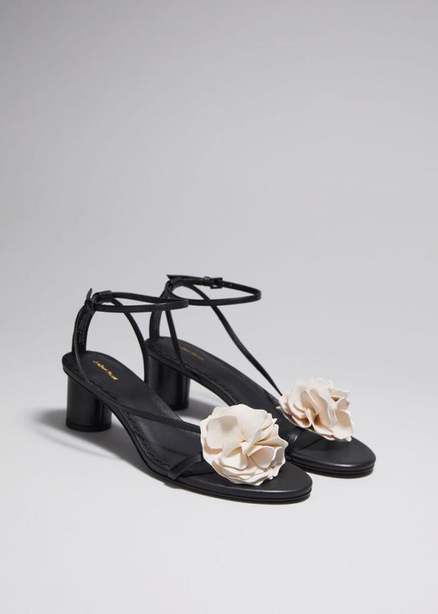 Ein Paar schwarze Sandalen mit cremefarbenen Blumenverzierungen stehen vor einem neutralen Hintergrund.