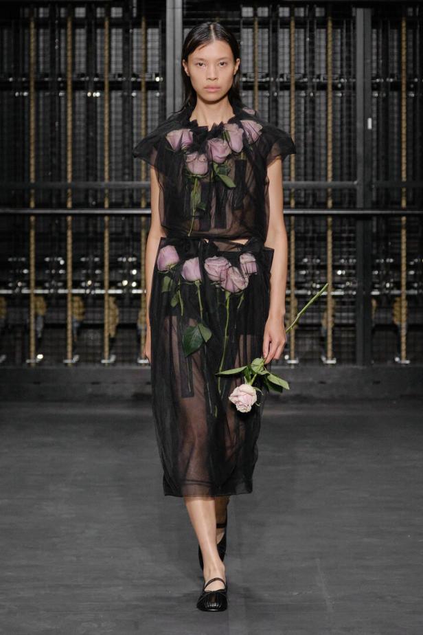Eine Frau in einem transparenten Kleid mit Rosen auf dem Laufsteg.