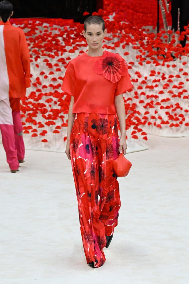 Ein Model in einem roten Ensemble mit Blumenmuster auf einem Laufsteg.