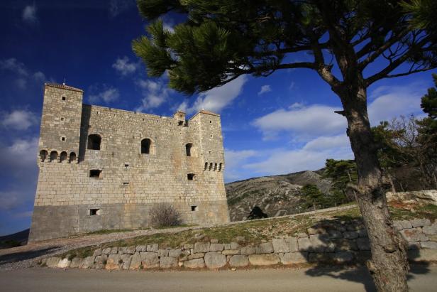 Eine mittelalterliche Burg aus Stein unter blauem Himmel mit Wolken.