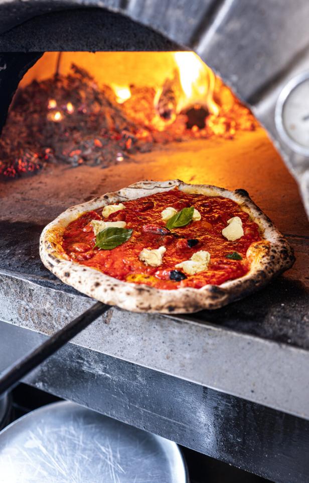 Eine Pizza mit Tomatensoße, Mozzarella und Basilikum wird in einem Holzofen gebacken.