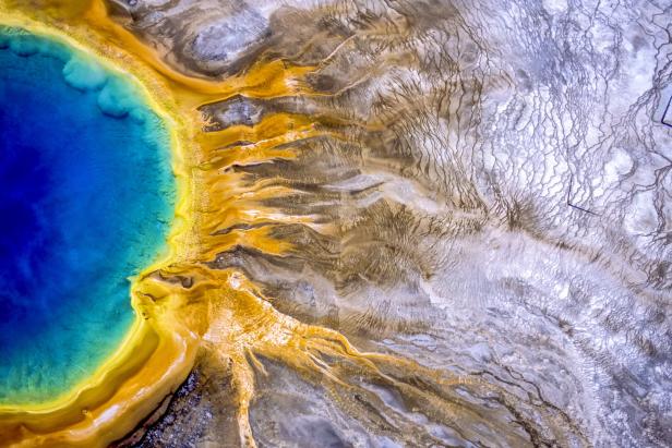 Luftaufnahme einer Thermalquelle mit blauem Wasser und gelben Ablagerungen.
