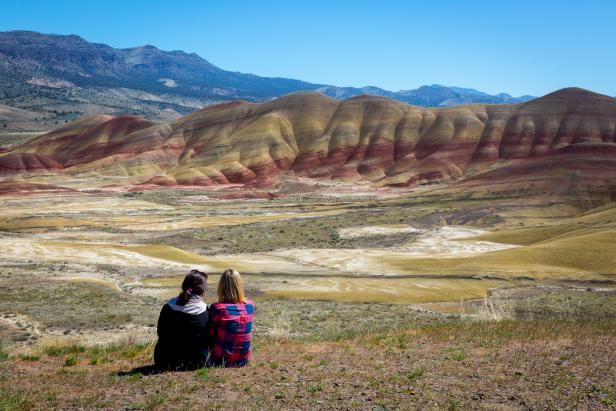 Zwei Frauen sitzen auf einem Hügel und blicken auf die Painted Hills in Oregon.