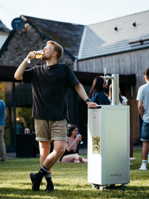 Ein Mann trinkt ein Glas Bier an einem mobilen Bierwagen im Freien.
