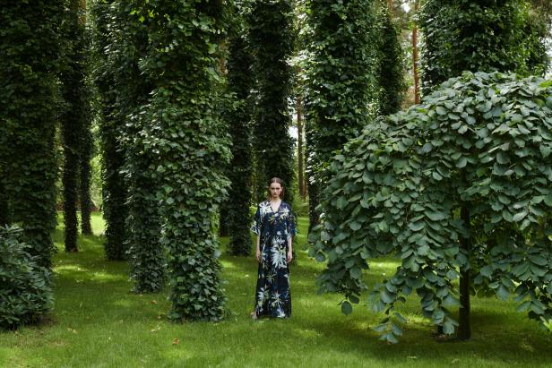 Eine Frau in einem langen Kleid steht in einem grünen Garten mit Bäumen.