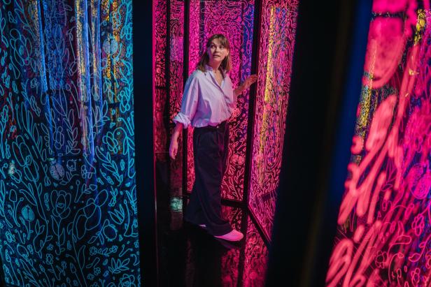 Eine Frau steht in einem Raum mit floralen Mustern in Neonfarben.