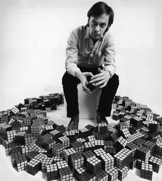 Ein Mann sitzt inmitten einer großen Anzahl von Rubik's Cubes und hält einen in den Händen.