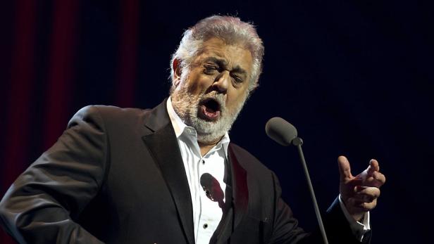 Plácido Domingo singt in einem schwarzen Anzug vor einem Mikrofon.