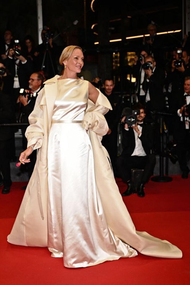 Uma Thurman auf dem roten Teppich in einem langen, hellen Kleid und Mantel.