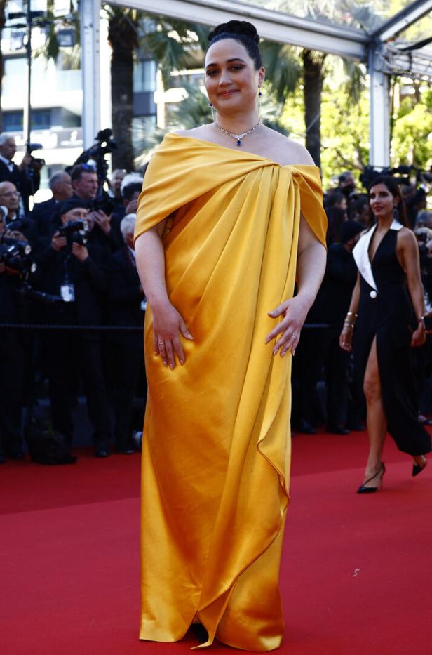 Eine Frau in einem goldfarbenen Kleid auf einem roten Teppich.