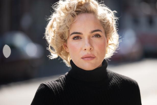 Porträt einer Frau mit blonden Locken und schwarzem Rollkragenpullover.