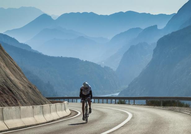 Ein Radfahrer fährt auf einer kurvenreichen Straße vor einer Bergkulisse.