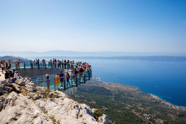 Viele Menschen auf einer gläsernen Aussichtsplattform mit Blick auf das Meer und die Küste.