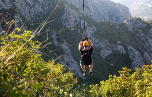 Ein Mann fährt mit einer Seilrutsche über eine grüne Berglandschaft.