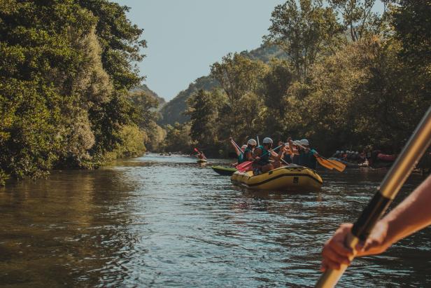 Eine Gruppe von Menschen raftet auf einem Fluss durch eine bewaldete Landschaft.