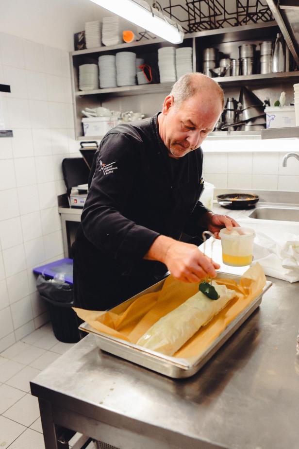 Ein Koch bestreicht einen Strudel in einer Restaurantküche mit flüssiger Butter.